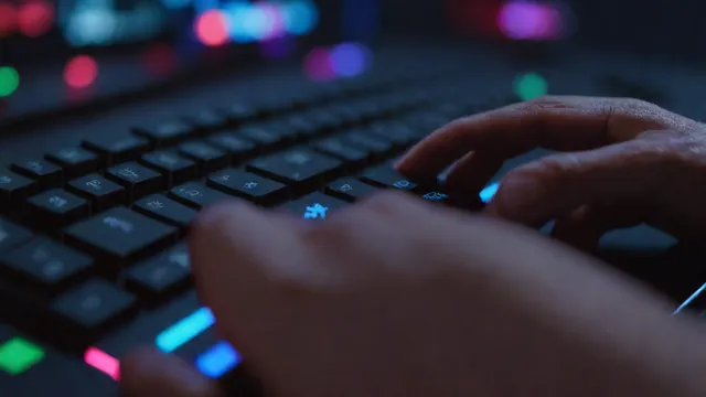 Mano sosteniendo una tarjeta de pago frente a un teclado de ordenador de videojuegos iluminado.