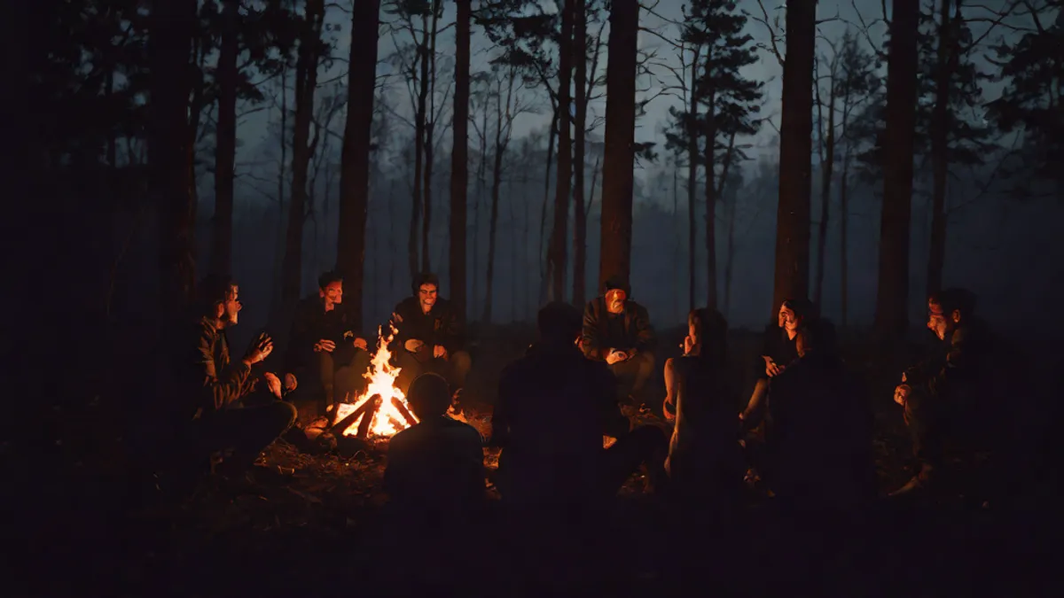 Grupo de personas sentadas alrededor de una fogata en el bosque de noche contando historias.