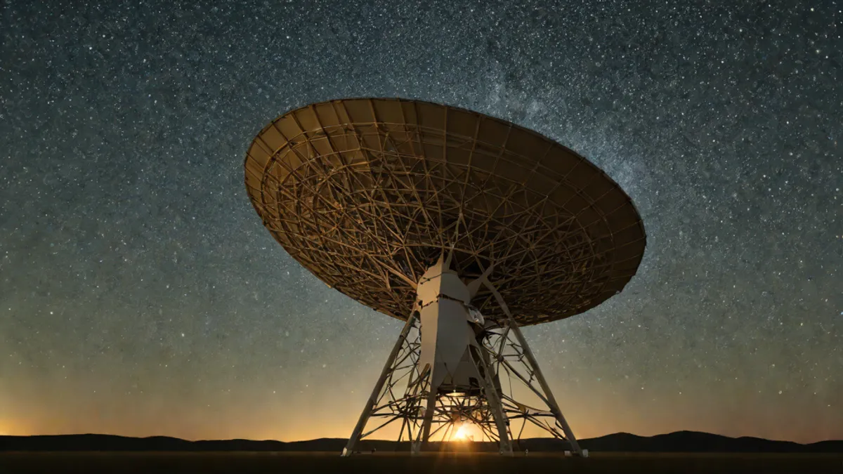 Radiotelescopio gigante apuntando al cielo nocturno estrellado en busca de señales en el universo.