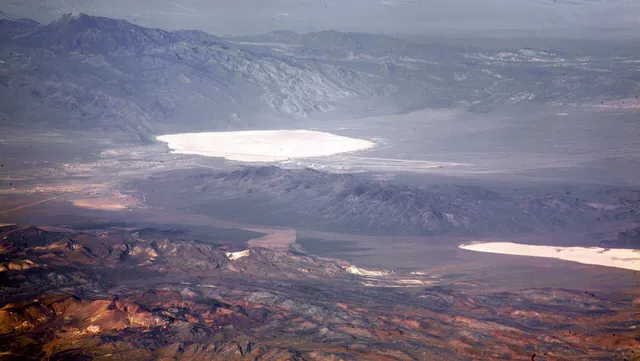 Valla de seguridad en el desierto de Nevada con hangares militares y la cuenca de Groom Lake al fondo.