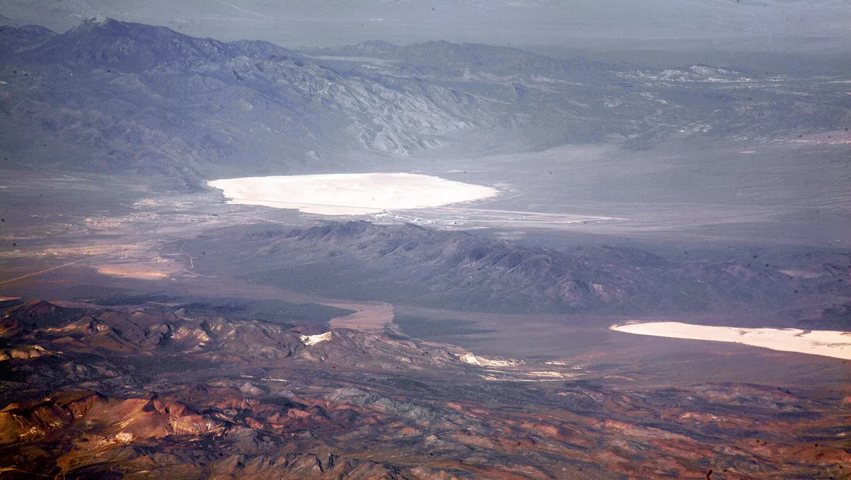 Valla de seguridad en el desierto de Nevada con hangares militares y la cuenca de Groom Lake al fondo.