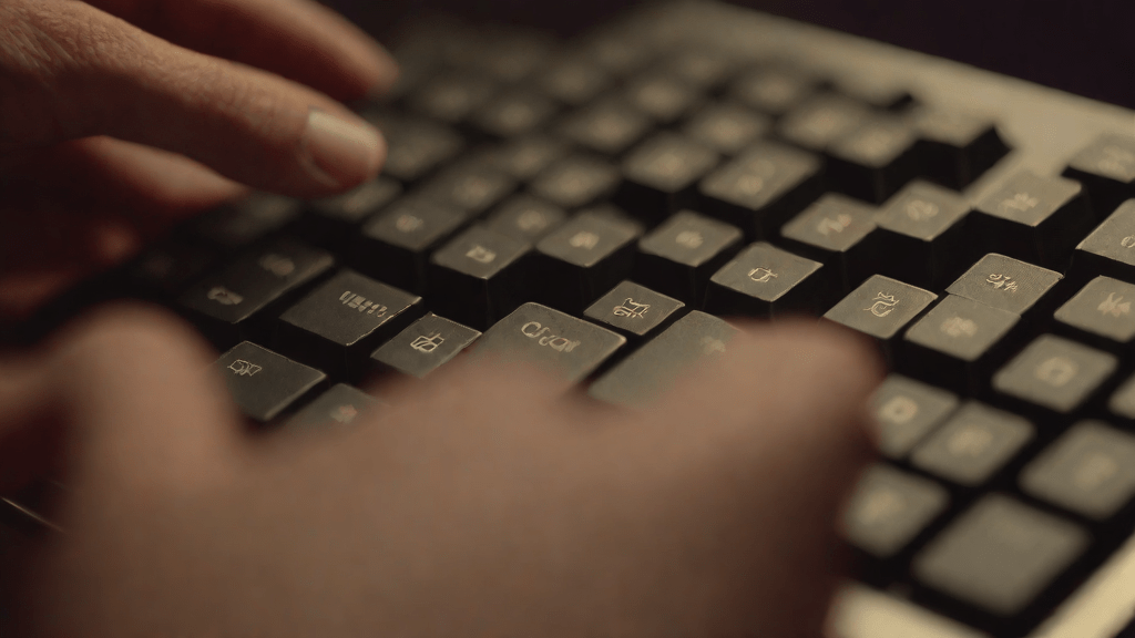Manos escribiendo en teclado mecánico en una biblioteca de noche